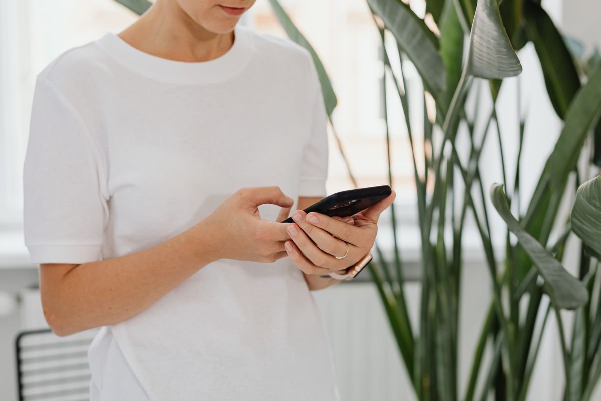 Woman using a phone indoors among houseplants — reminder UIs organise tasks; they do not sense pot moisture