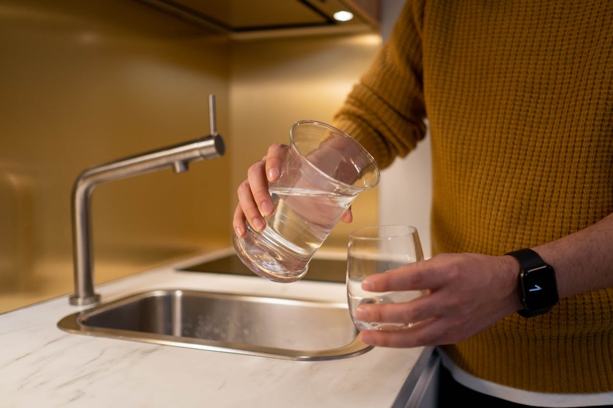 Person pouring water from a pitcher into a glass in a contemporary kitchen