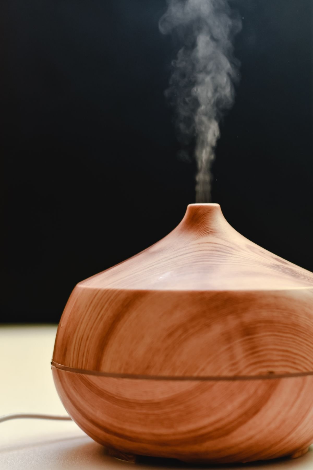 A wooden diffuser releasing steam against a dark background