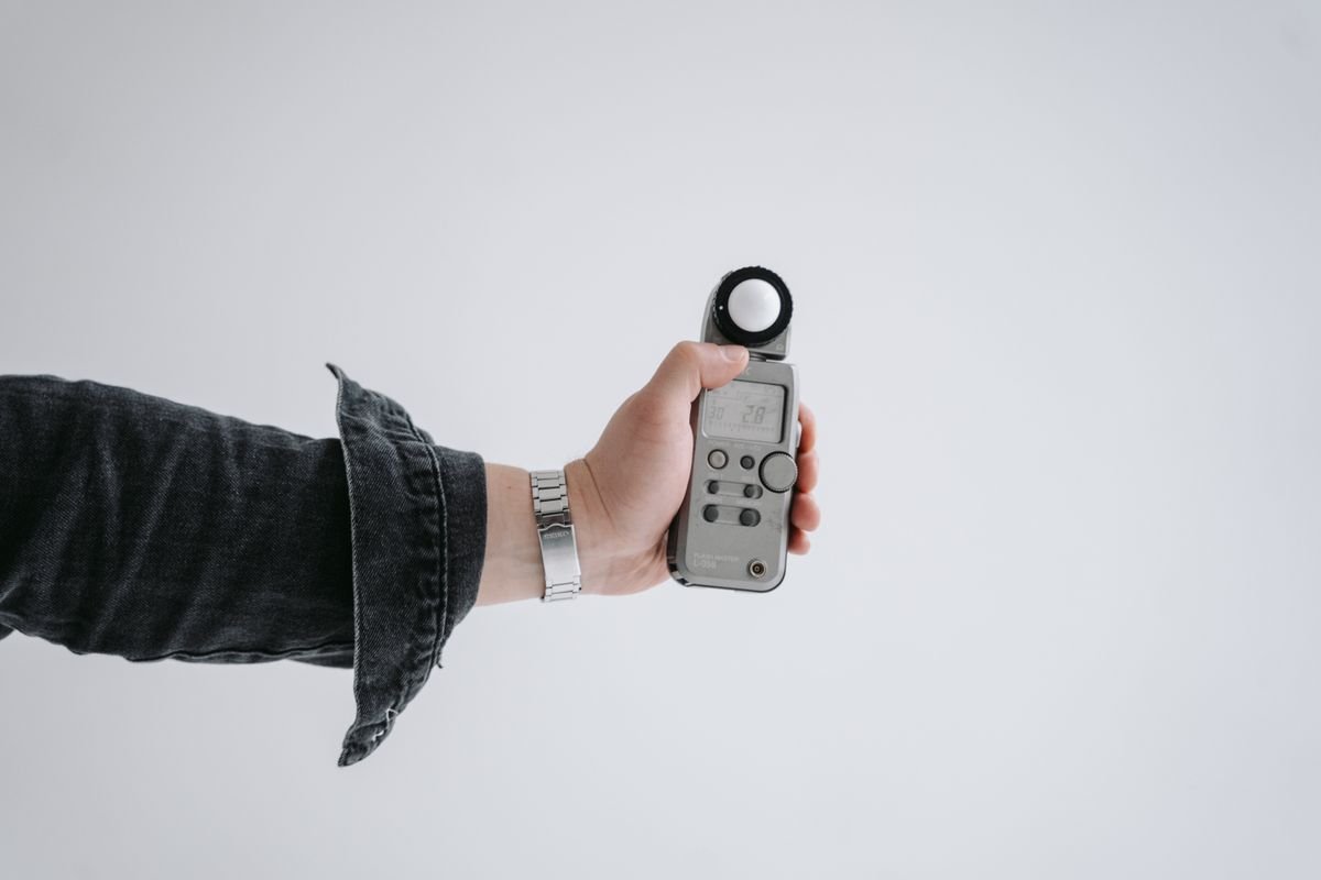 Hand holding a light meter in a minimal setting — quantify Peperomia leaf illuminance in lux or foot-candles
