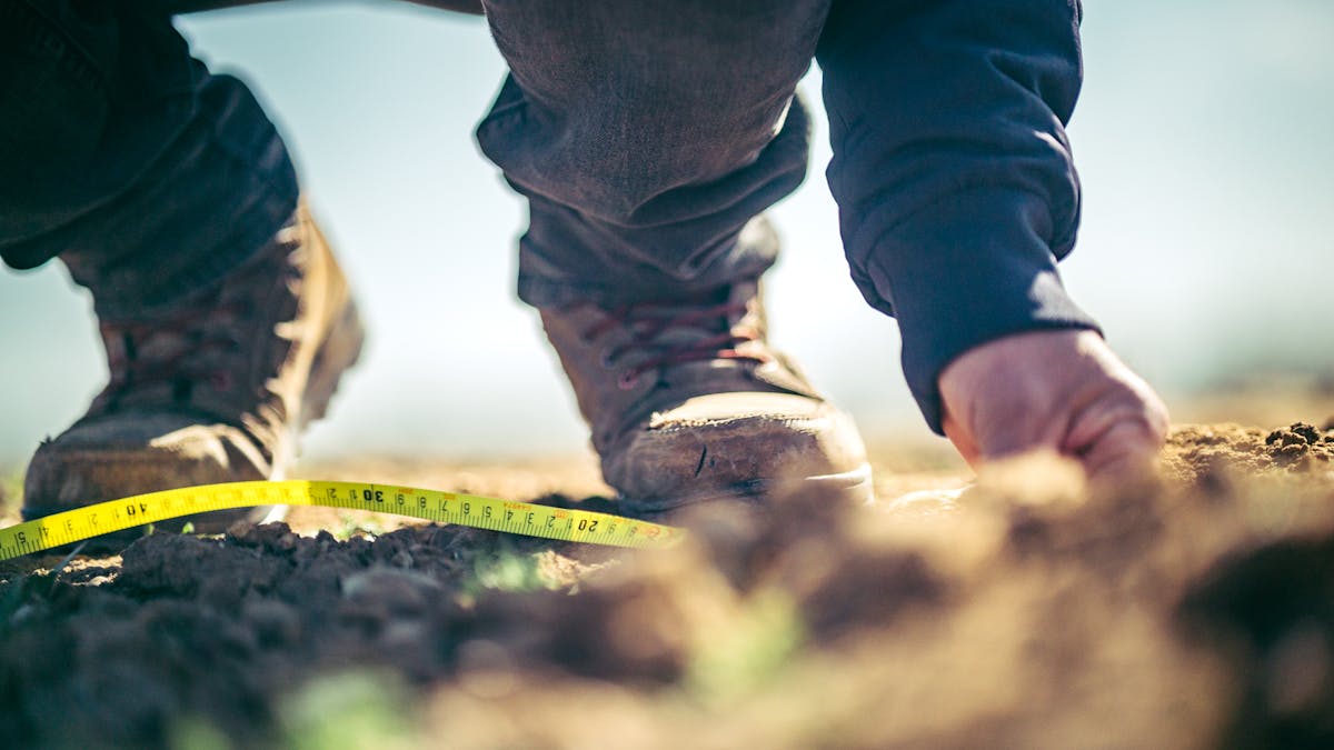 Person in boots measuring soil with tape outdoors