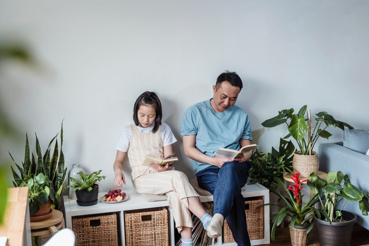 Parent and child reading at home surrounded by houseplants — non-toxic chemistry still means keep thick leaves out of toddler mouths