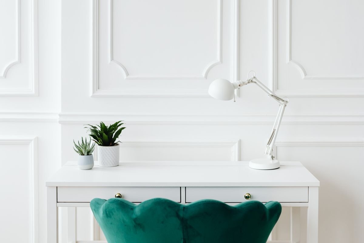 A minimalist desk setup with a white desk lamp and potted plant, illustrating supplemental office lighting