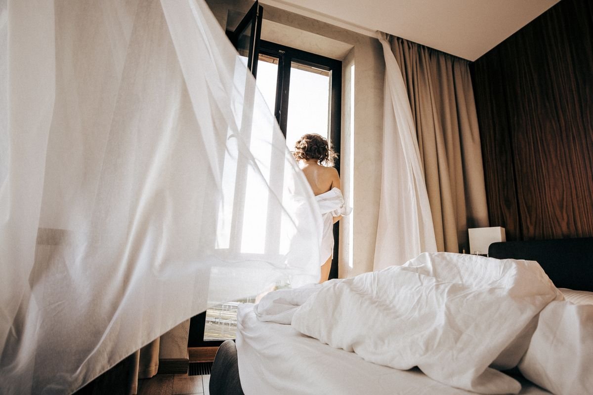 Person opening curtains at a bright window — outdoor air exchange that outperforms peperomia air purification claims